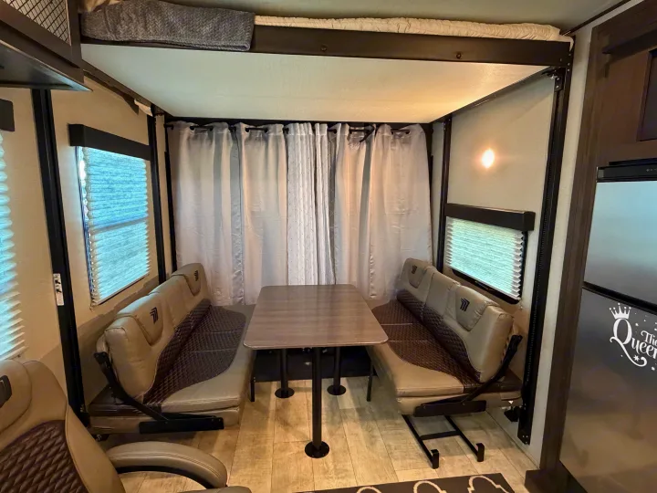 Comfortable RV rental interior featuring a dinette setup with a table, benches, and a top bunk bed.. Grand Design Momentum Toy Hauler 2022