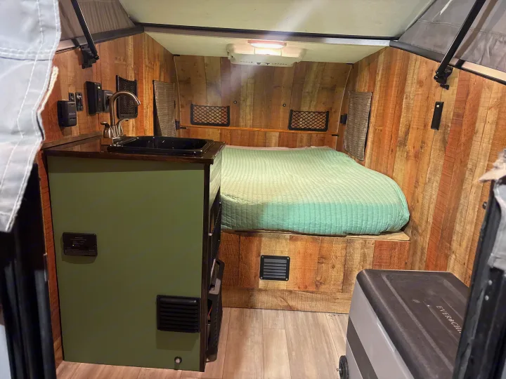 Cozy rv rental interior: green bed, small kitchen sink, wood walls, and control panel, ideal for compact travel.. Forest River Viking TD 2022