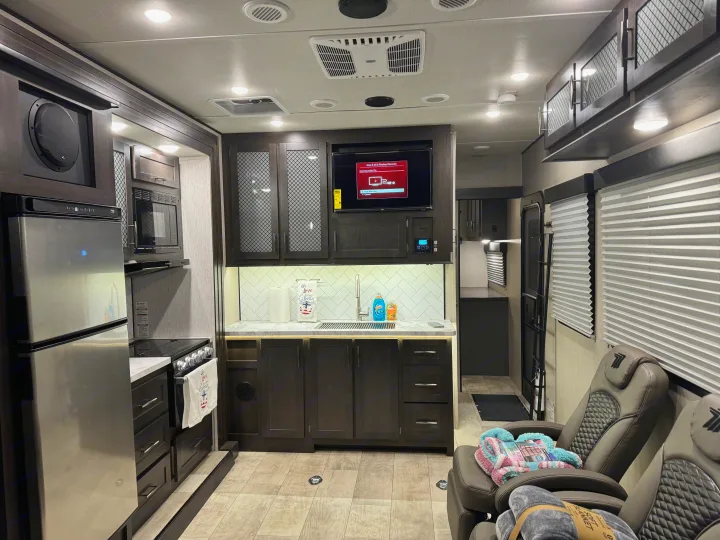 Spacious RV rental interior: a modern kitchen with stainless steel appliances, dark cabinets, a sink, and a cozy living area with recliners.. Grand Design Momentum Toy Hauler 2022