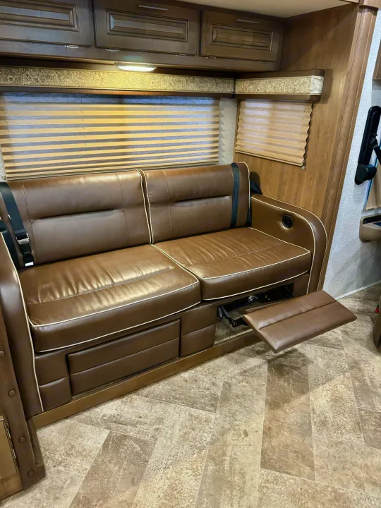 RV rental interior: brown leather recliner sofa with extended footrest, patterned valance, and overhead cabinets.. Georgetown GT3 2019