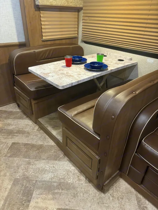 RV rental dinette: cozy brown benches with white trim face a patterned table, set with colorful dishes.. Georgetown GT3 2019