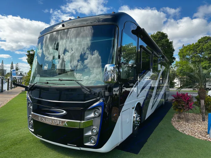 Sleek black and white luxury Entegra motorhome RV rental parked on green grass. Clouds reflect in its windows by a dock.. Entegra Coach Reatta 2021