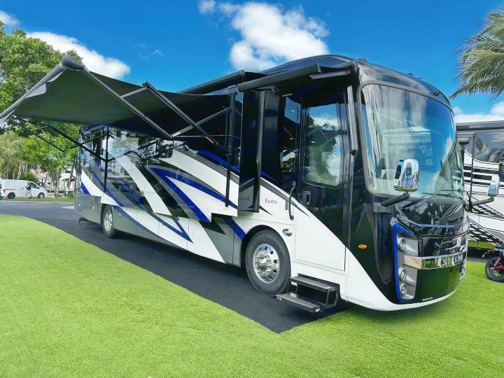 Luxurious Entegra Reatta RV in black, white & blue with extended awning, parked on green turf. Great for a premium rv rental.. Entegra Coach Reatta 2021