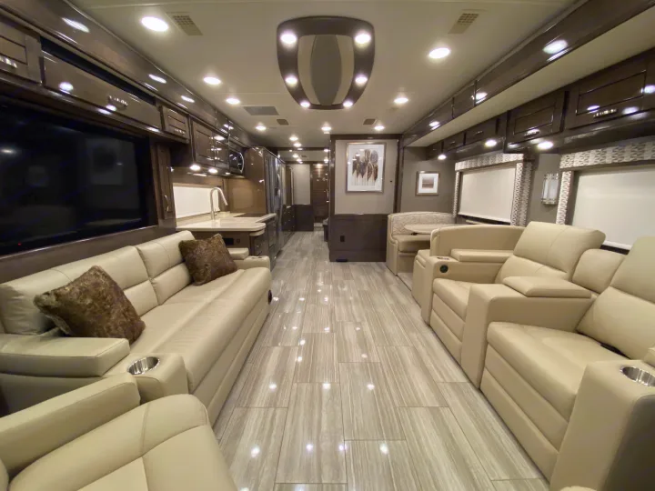 Spacious luxury rv rental interior with opposing cream-colored seating, modern kitchen, and dining area for comfortable travel.. Entegra Coach Reatta 2021