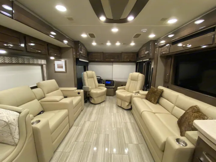 Experience this luxurious RV rental interior with cream leather seating, sleek wood cabinetry, and a modern tiled floor, offering spacious comfort.. Entegra Coach Reatta 2021