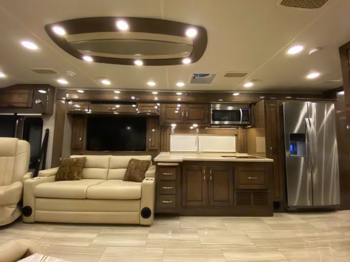 Modern RV rental interior with a spacious kitchen, comfortable sofa, TV, and fridge. Ideal for road trips.. Entegra Coach Reatta 2021
