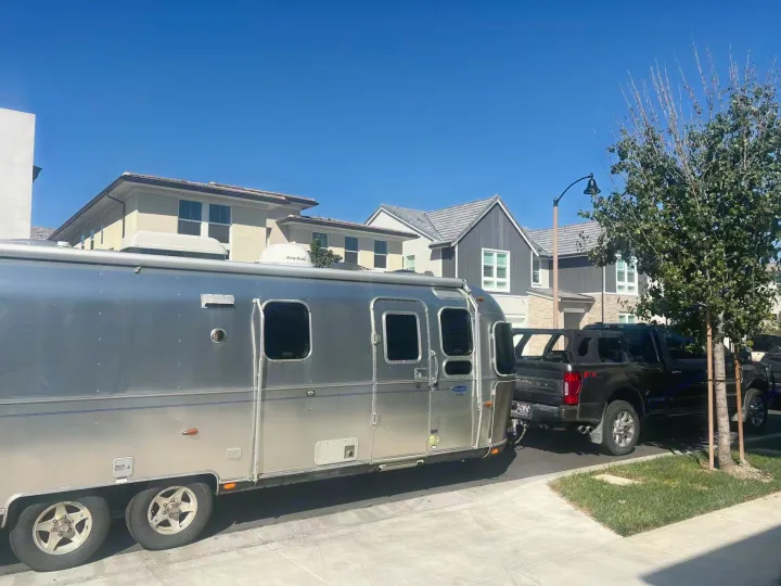 Silver Airstream travel trailer, an RV rental, hitched to a black pickup truck parked on a sunny suburban street.. Airstream Classic 2012