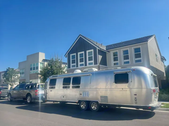 A silver Airstream rv rental is hitched to a grey pickup truck, parked curbside under a clear blue sky. Ready for travel.. Airstream Classic 2012