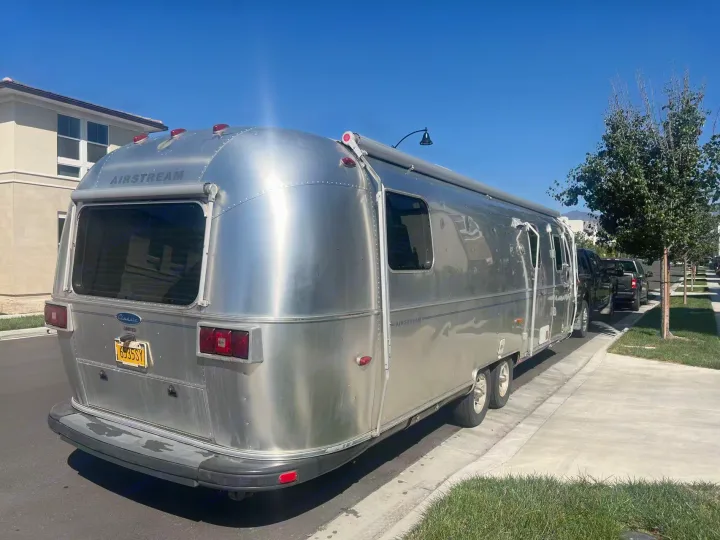 A sleek silver Airstream travel trailer, ideal for an RV rental, parked curbside on a sunny day.. Airstream Classic 2012