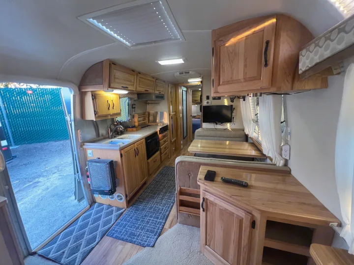 Inside this bright RV rental, a well-equipped kitchen, dining area with tables and benches, and modern wooden cabinetry are visible.. Airstream Classic 2012
