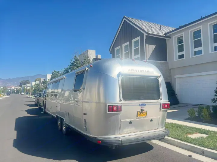 A sleek silver Airstream RV, potentially an rv rental, parked on a sunny residential street next to a modern home.. Airstream Classic 2012
