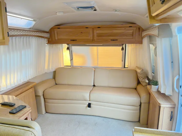 Cozy RV rental living room with a beige sofa, wooden cabinets, and bright windows, perfect for relaxation on the road.. Airstream Classic 2012