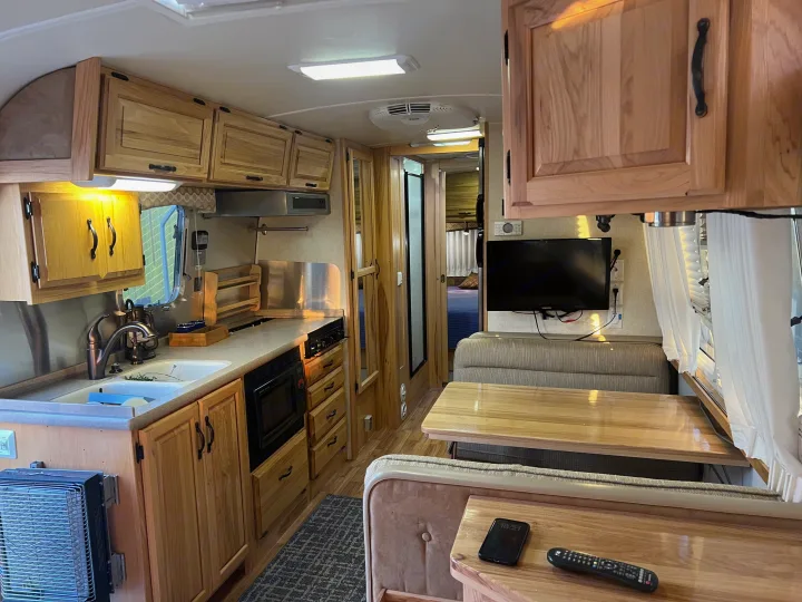 rv rental: Cozy RV interior with a compact kitchen, dinette, and TV, featuring warm wooden cabinetry and light colors.. Airstream Classic 2012