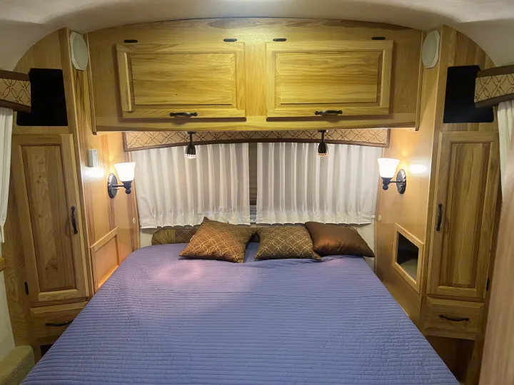 Cozy RV rental bedroom featuring wooden cabinets, a comfortable bed with a blue quilt, and warm lighting.. Airstream Classic 2012