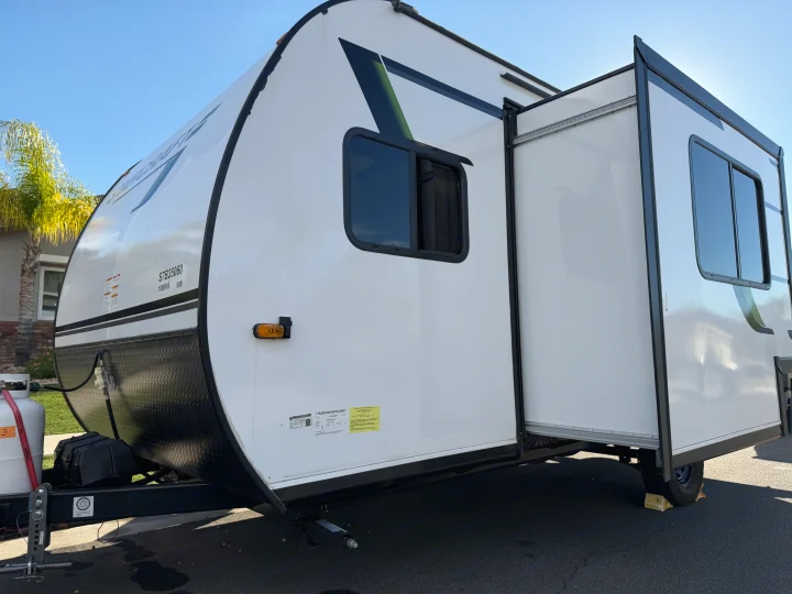 White rv rental travel trailer with an extended slide-out and front propane tank, parked outdoors on a sunny day.. Autumn Ridge 188BHS 2025