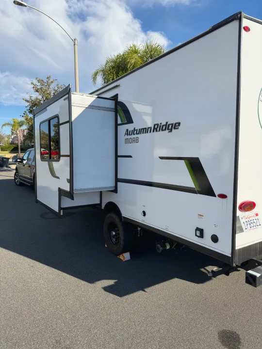 White Autumn Ridge MOAB rv rental, a travel trailer with an open side panel, parked on asphalt displaying utilities.. Autumn Ridge 188BHS 2025