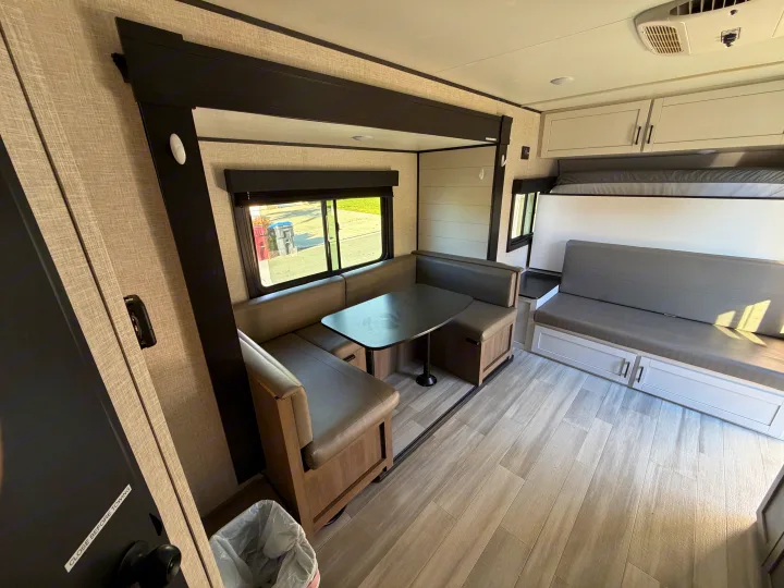 Modern rv rental interior with a U-shaped dinette, table, and a versatile sofa that converts to a bunk bed.. Autumn Ridge 188BHS 2025