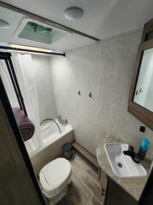 Inside an RV rental bathroom: a shower with curtain, toilet, sink, and mirror. Compact yet complete facilities.. Gulf Stream Ameri-Lite Super Lite 2022