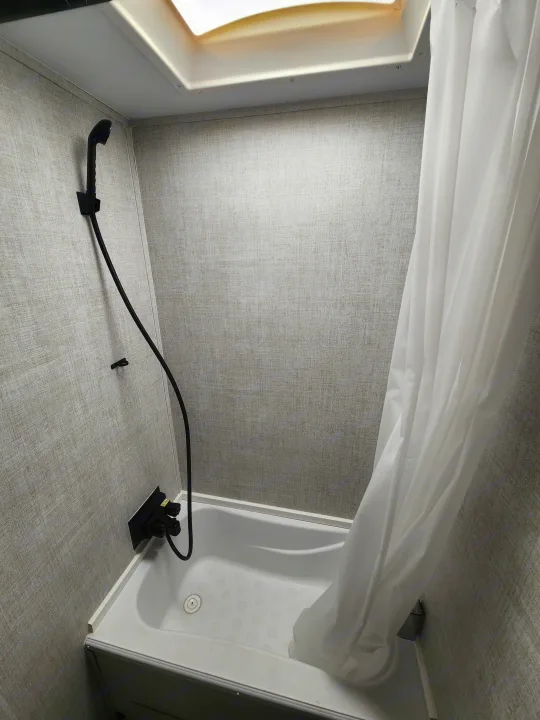 Explore this compact RV rental shower, featuring a white tub, textured walls, black shower head, and bright skylight.. Gulf Stream Ameri-Lite Super Lite 2022