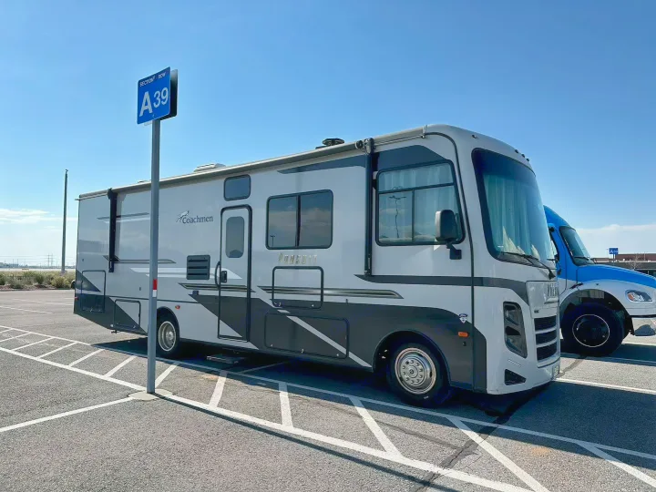 A grey Coachmen Pursuit rv rental is parked in section A39 of a sunny lot, with a blue truck next to it.. Coachmen Pursuit 31BH 2023