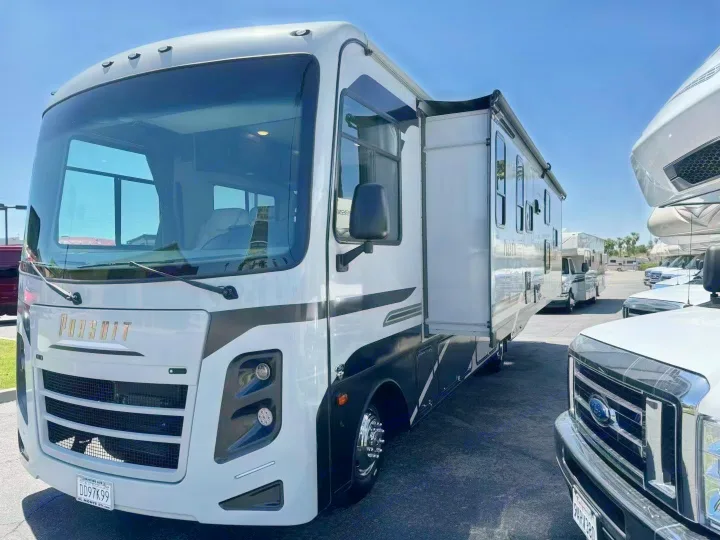 A white Class A Pursuit RV with black accents, slide-out extended, is parked on a sunny lot, ideal for rv rental adventures.. Coachmen Pursuit 31BH 2023