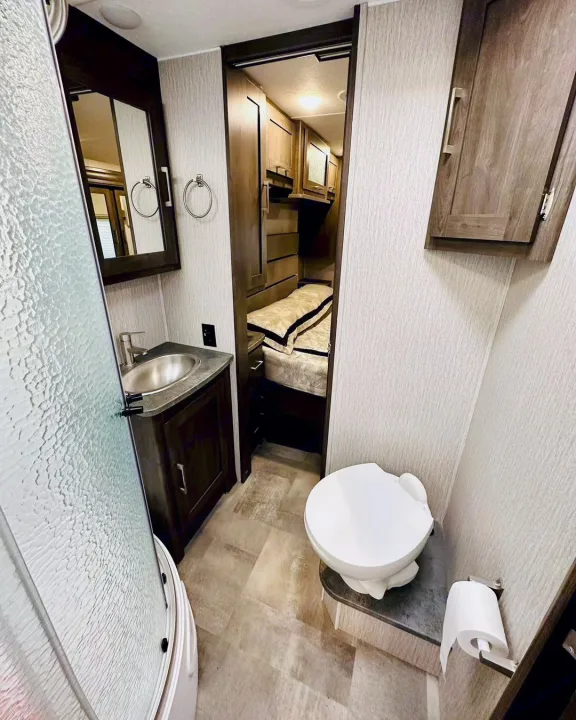This RV rental features a compact bathroom with a shower, sink, and toilet, leading to a cozy bedroom with bunk beds.. Coachmen Pursuit 31BH 2023