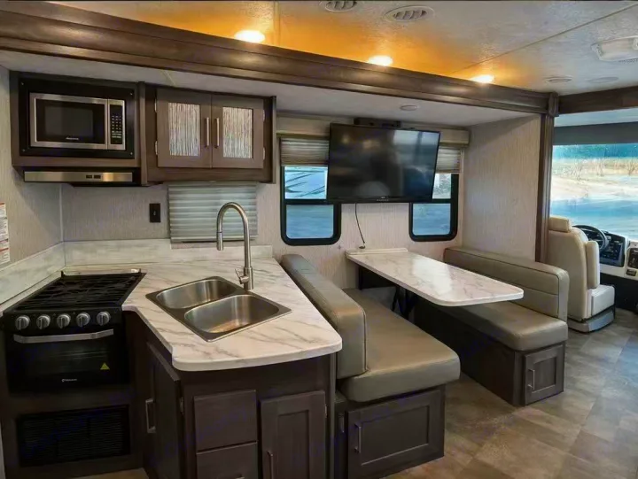 Modern rv rental kitchen & dinette: microwave, stove, double sink, and bench seating with a TV.. Coachmen Pursuit 31BH 2023