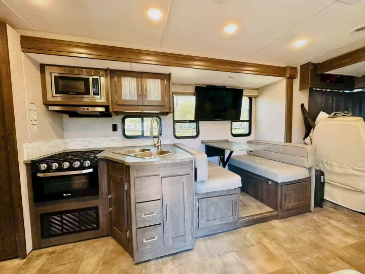 Comfortable RV rental interior features a well-equipped kitchen with stove, sink, microwave, and a cozy dinette with TV.. Coachmen Pursuit 31BH 2023