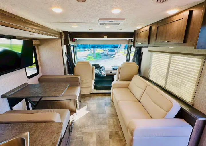 Spacious RV rental interior featuring a modern cockpit, cream sofa, dinette, and TV, perfect for comfortable travel.. Coachmen Pursuit 31BH 2023