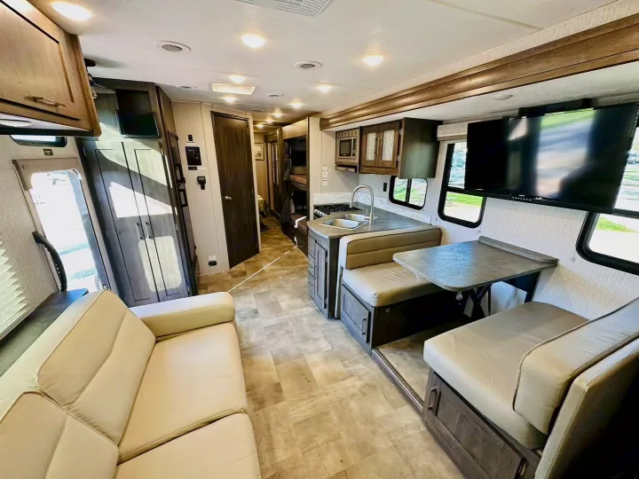 Spacious rv rental interior featuring a modern living area with a couch, kitchen, dinette, and bunk beds. Bright and inviting for travel.. Coachmen Pursuit 31BH 2023