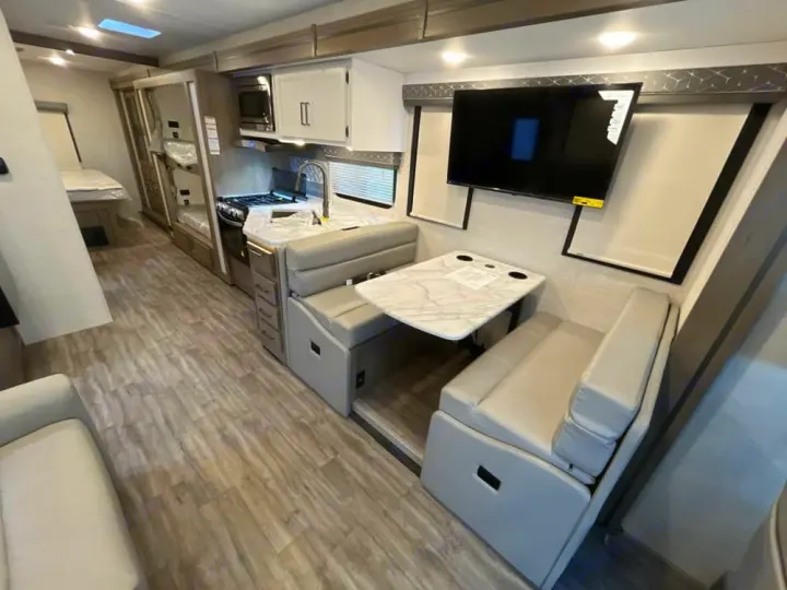 Inside a bright RV rental: a full kitchen, comfy dinette, living area, and bunk beds for travelers.. Thor Freedom Traveler 2025