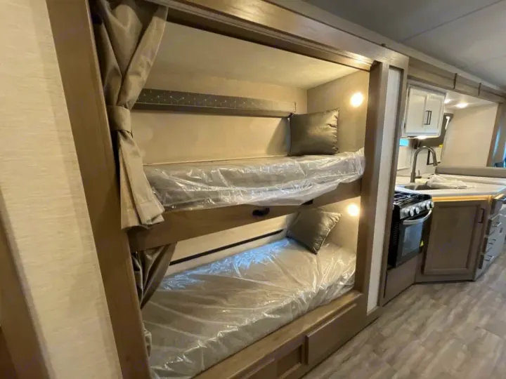 RV rental: Bunk beds with curtains & plastic-covered mattresses. Nearby kitchen has stove, sink, and cabinets. Great for family travel.. Thor Freedom Traveler 2025