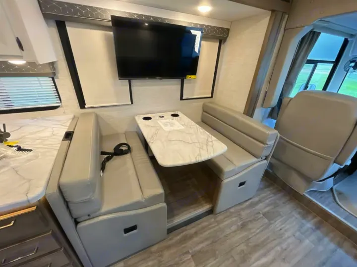 Modern RV rental interior featuring a dinette with seating, wall-mounted TV, and a glimpse of the kitchen area.. Thor Freedom Traveler 2025