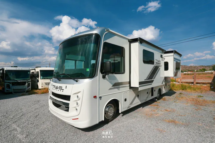 This sleek white and silver RV rental, with slide-outs extended, stands in a gravel lot under a blue, cloudy sky.. Jayco Travel Supreme A Series 27A 2025