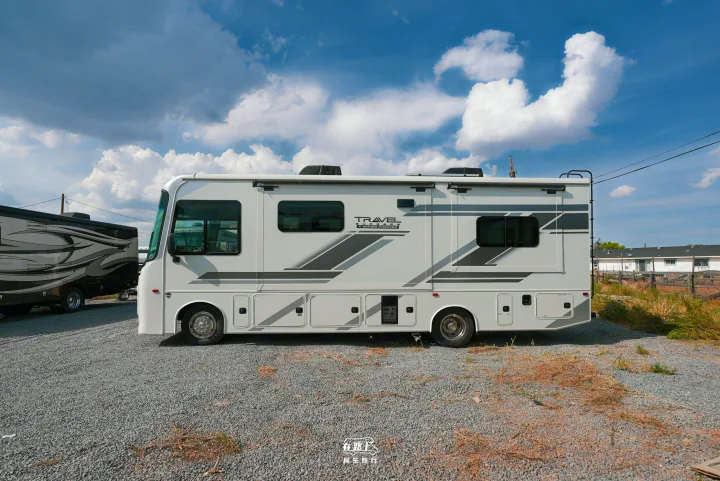 This white Class A RV rental is parked on a gravel lot under a partly cloudy sky, with another RV in the background.. Jayco Travel Supreme A Series 27A 2025