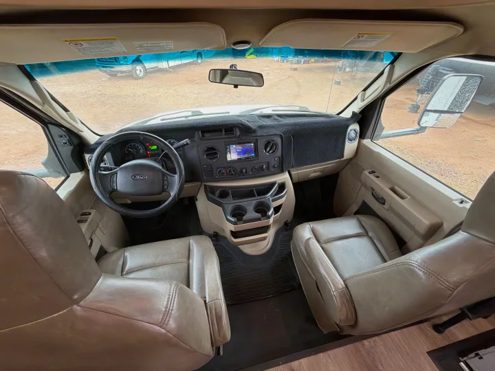 Interior of an RV rental front cab: Ford steering wheel, navigation screen, tan leather seats, and outdoor view.. Forest River Sunseeker 2017