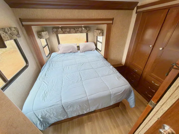 An RV rental bedroom with a large bed, light blue comforter, multiple windows, and ample wooden wardrobe storage.. Forest River Sunseeker 2017