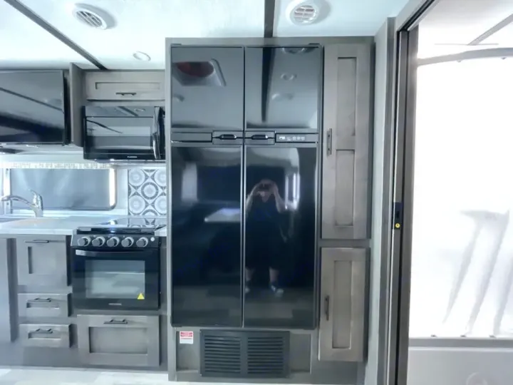 This RV rental kitchen features a modern fridge, stove, microwave, and grey cabinets, offering amenities for your travel.. FR3 FR3 Motorhome 2024