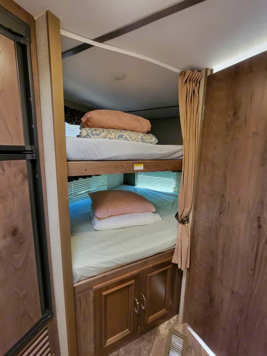 RV rental sleeping area with cozy bunk beds, bedding, window blinds, and storage cabinets.. Keystone RV Passport Grand Touring 2018