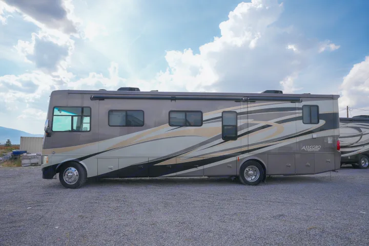 RV rental: Grey Tiffin Allegro motorhome with graphic stripes, parked on gravel under a cloudy sky.. Allegro Allegro Motorhome 2014