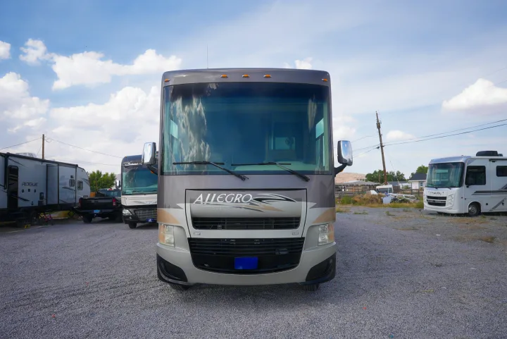 Front view of a grey Allegro Open Road RV rental (motorhome) on a gravel lot, surrounded by other RVs and a pickup.. Allegro Allegro Motorhome 2014