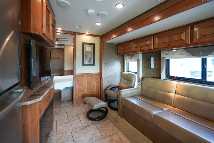Luxurious RV rental interior: spacious living area with a sofa, recliner, TV, wood cabinetry, and a view into the bedroom.. Allegro Allegro Motorhome 2014