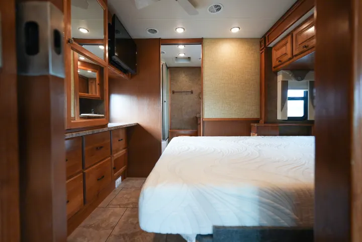 Step inside this inviting RV rental bedroom featuring a pristine bed, wooden cabinetry, vanity, and a private bathroom.. Allegro Allegro Motorhome 2014