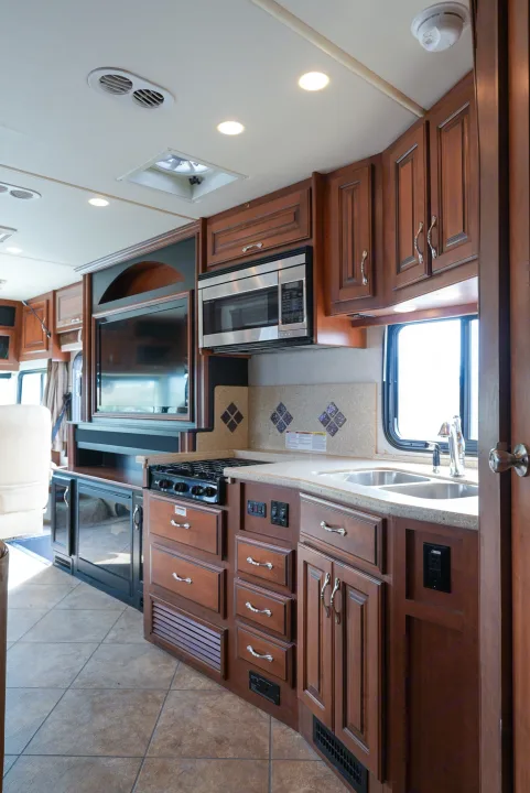 Modern RV rental kitchen with dark wood cabinets, a stove, microwave, double sink, and built-in TV area.. Southwind Southwind Motorhome 2013