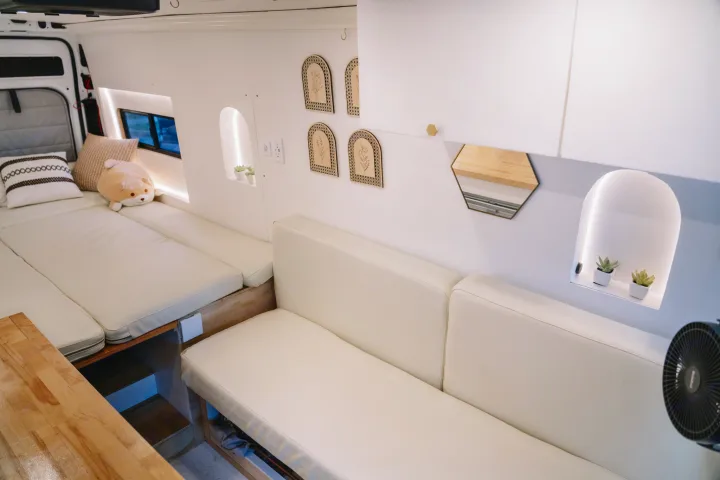 Cozy, modern RV rental interior featuring a bright white van space, cream cushions on bed and seating, minimalist decor, and soft lighting.. Ram ProMaster 3500 2024
