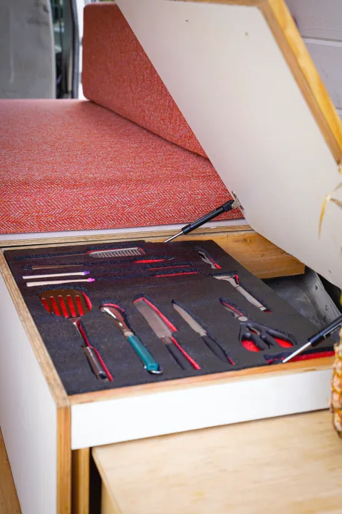 Custom-cut foam organizes kitchen utensils (spatula, knives) in a clever pull-out drawer under a red seat, ideal for an RV rental.. Ford Econolline 250s 2005