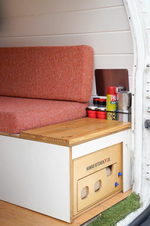 RV rental interior: cozy orange bench, Nomad Kitchen Co. pull-out kitchen, and essentials in a camper van.. Ford Econolline 250s 2005