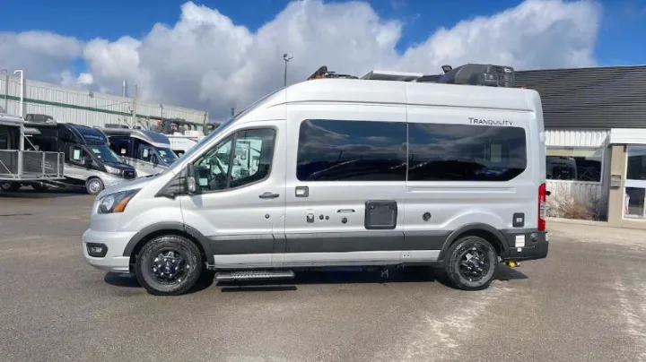 A silver Ford Transit Tranquility camper van, ideal for your next RV rental adventure, is parked at an outdoor lot.. Thor Motor Coach tranquility 2023