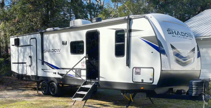 Side view of a white Shadow Cruiser travel trailer RV rental, with blue graphics, parked outdoors. Ready for your next adventure!. Cruiser RV Shadow Cruiser 2025