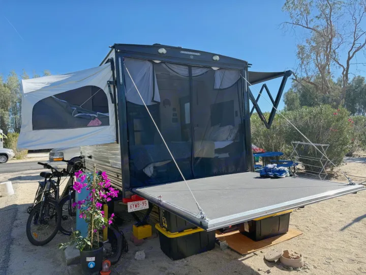 Spacious rv rental toy hauler with pop-out bed and ramp patio for outdoor camping setup, bikes nearby.. Sun Lite 14 THX 2026